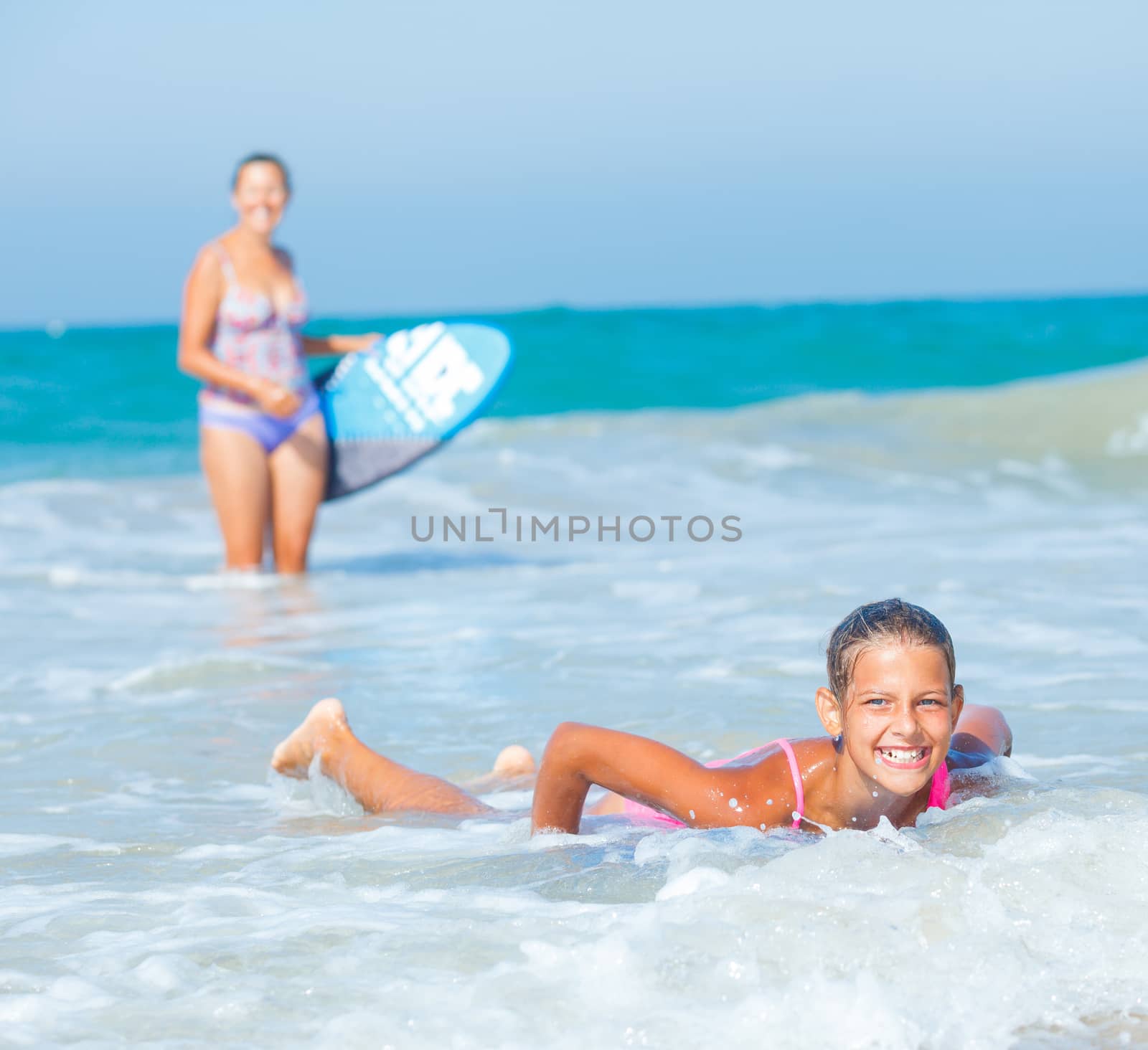 Summer vacation - Happy cute girl and her mother having fun with surfboard in the ocean