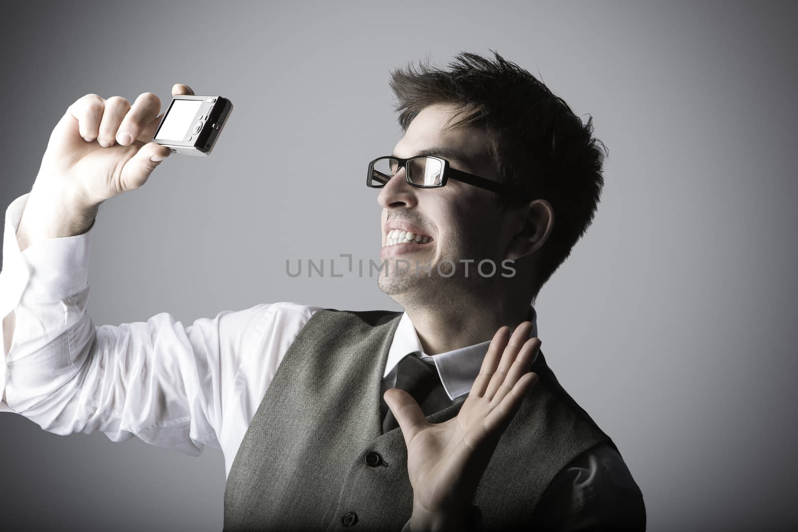 Laughing young man makes a selfie with a compact camera against grey background