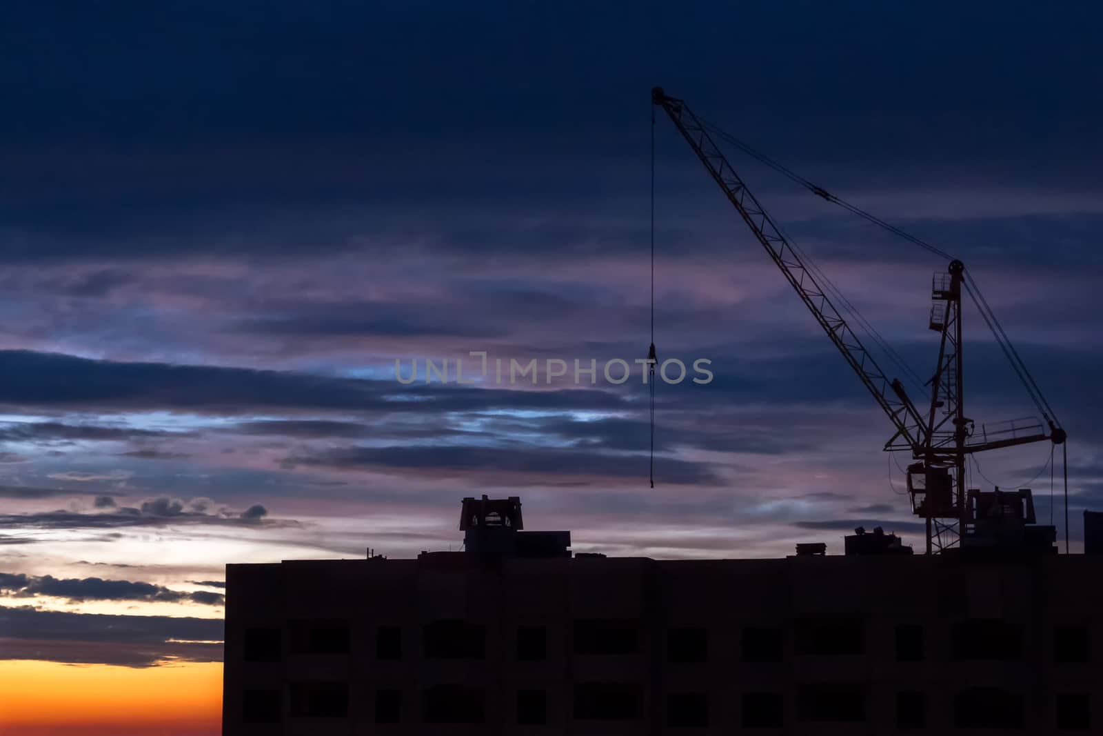 Silhouette of construction crane on dramatic sky background at the sundown