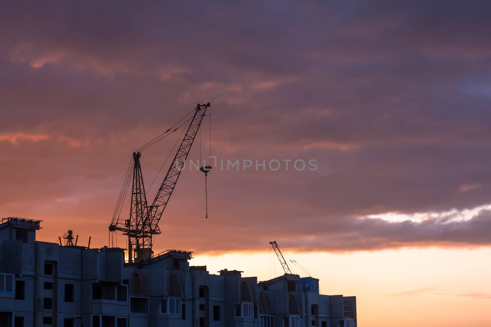 Silhouette of construction crane on dramatic sky background at the sundown