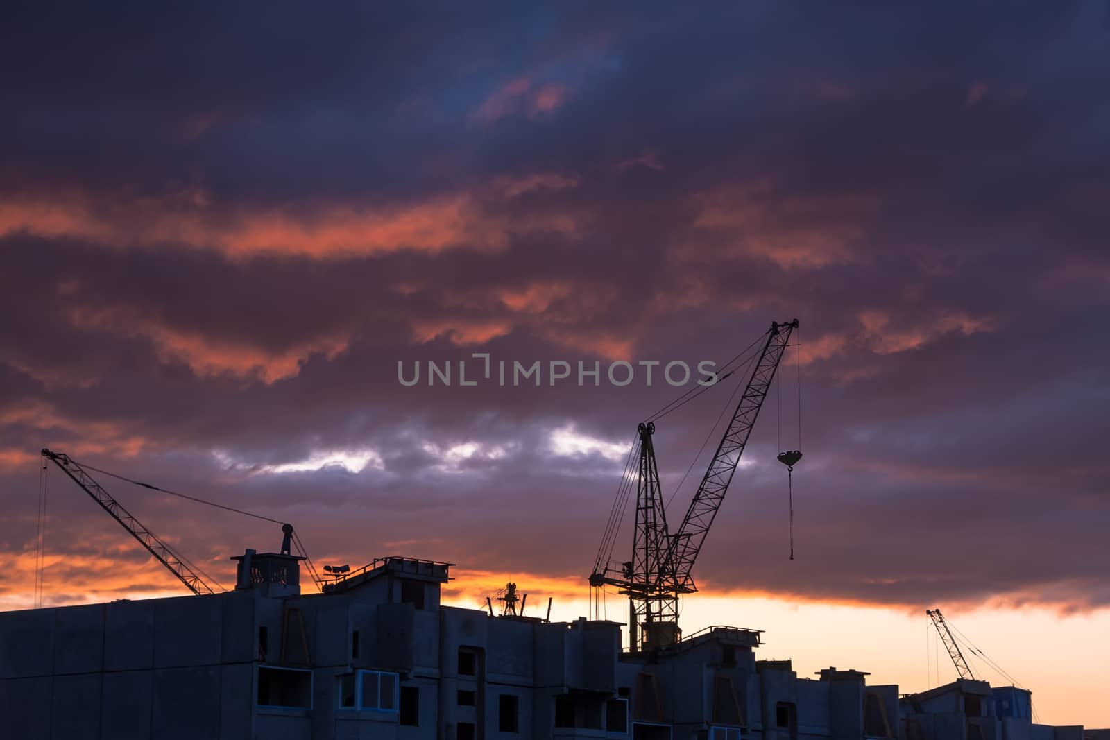 Silhouette of construction crane on dramatic sky background at the sundown
