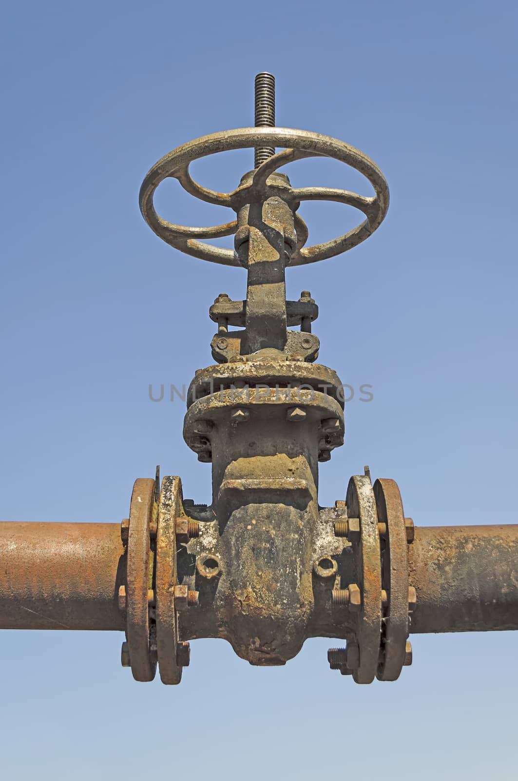 Old water pipe with large valve on blue sky background