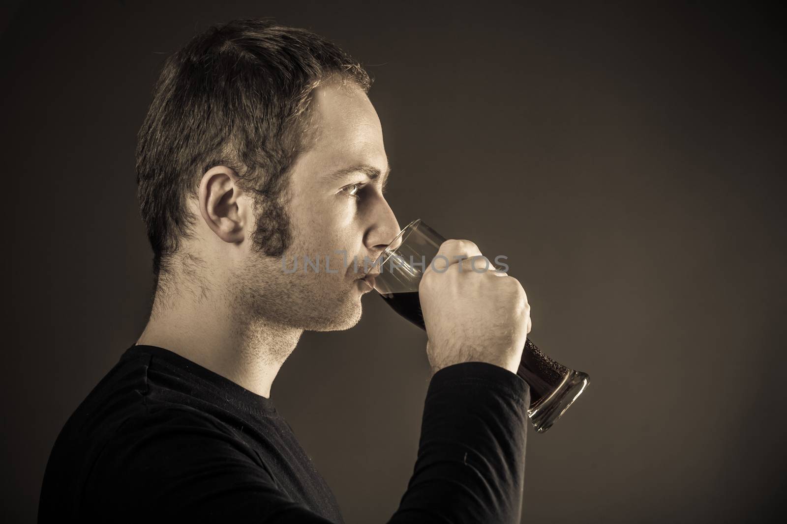Man drinking beer on dark background. Closeup