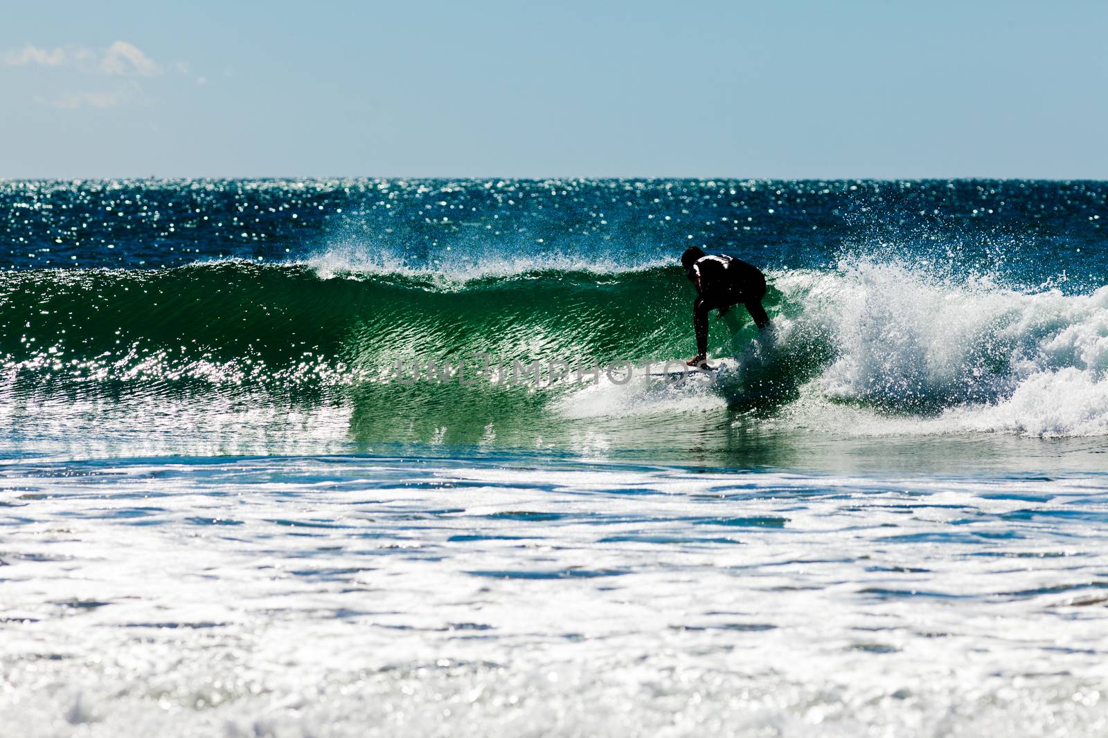 Surfer riding big ocean wave on surfboard as it starts to break with spray flying