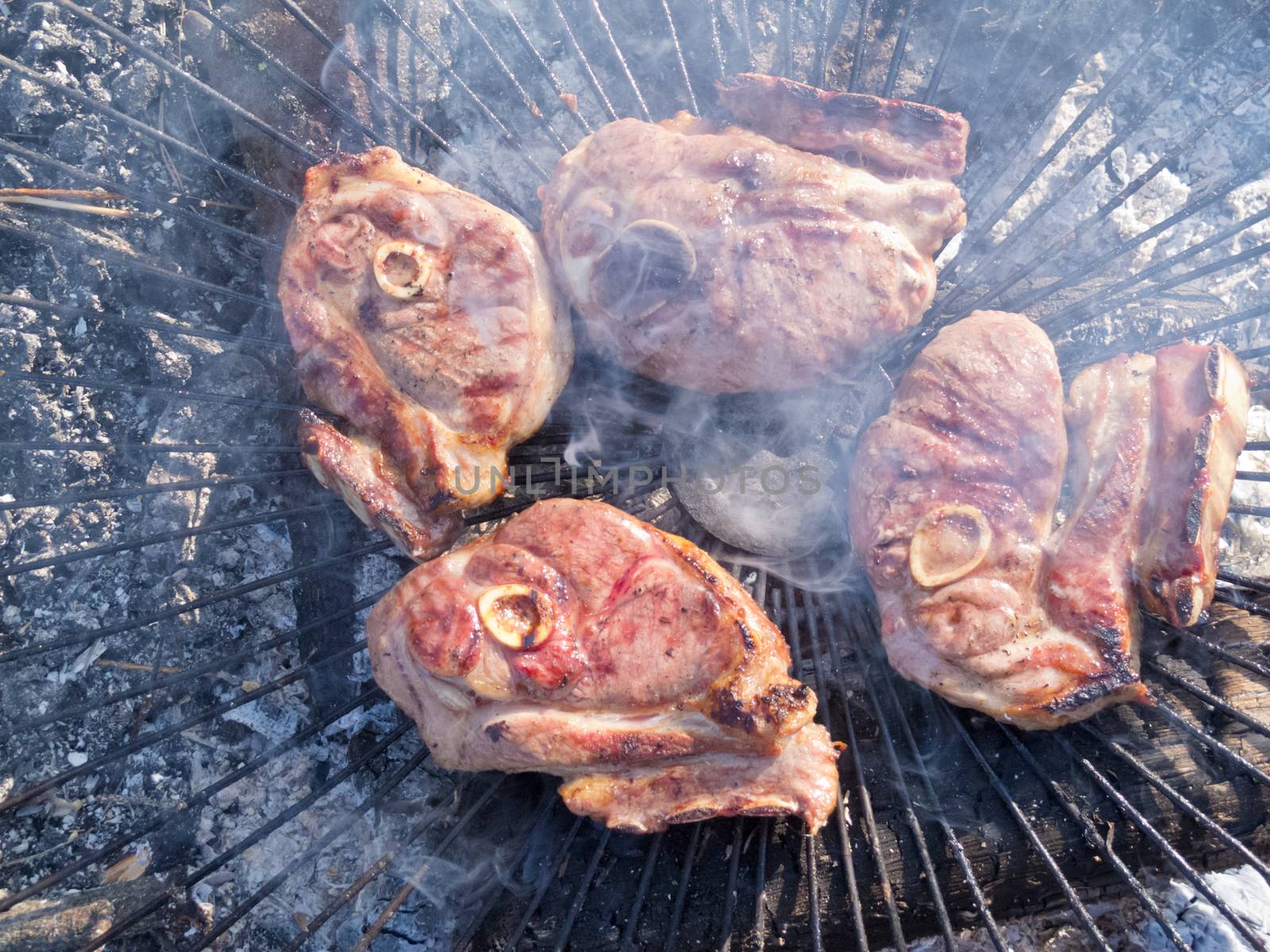 Crispy brown pork meat steaks grill over hot coals of bbq wood fire on metal grate grid