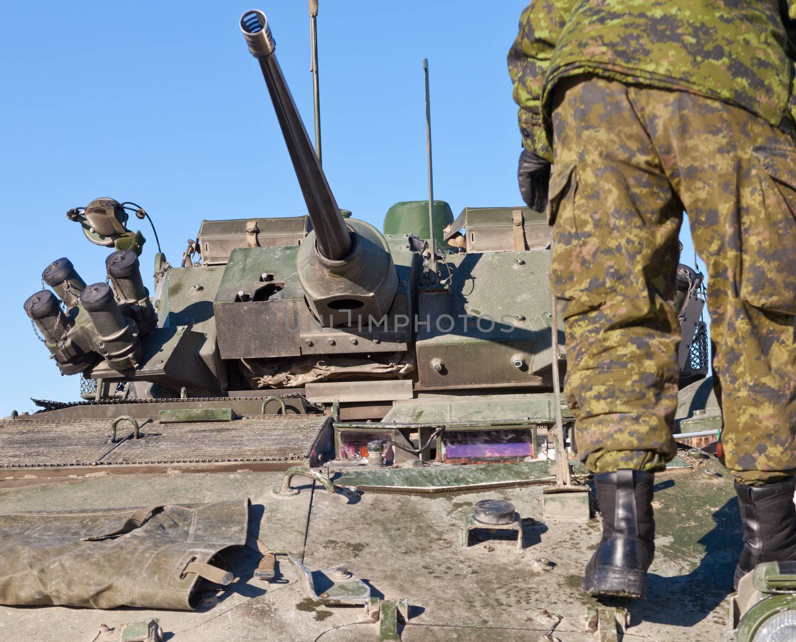Soldier in combat uniform standing on operational military armored tank vehicle with turret, armaments and gun