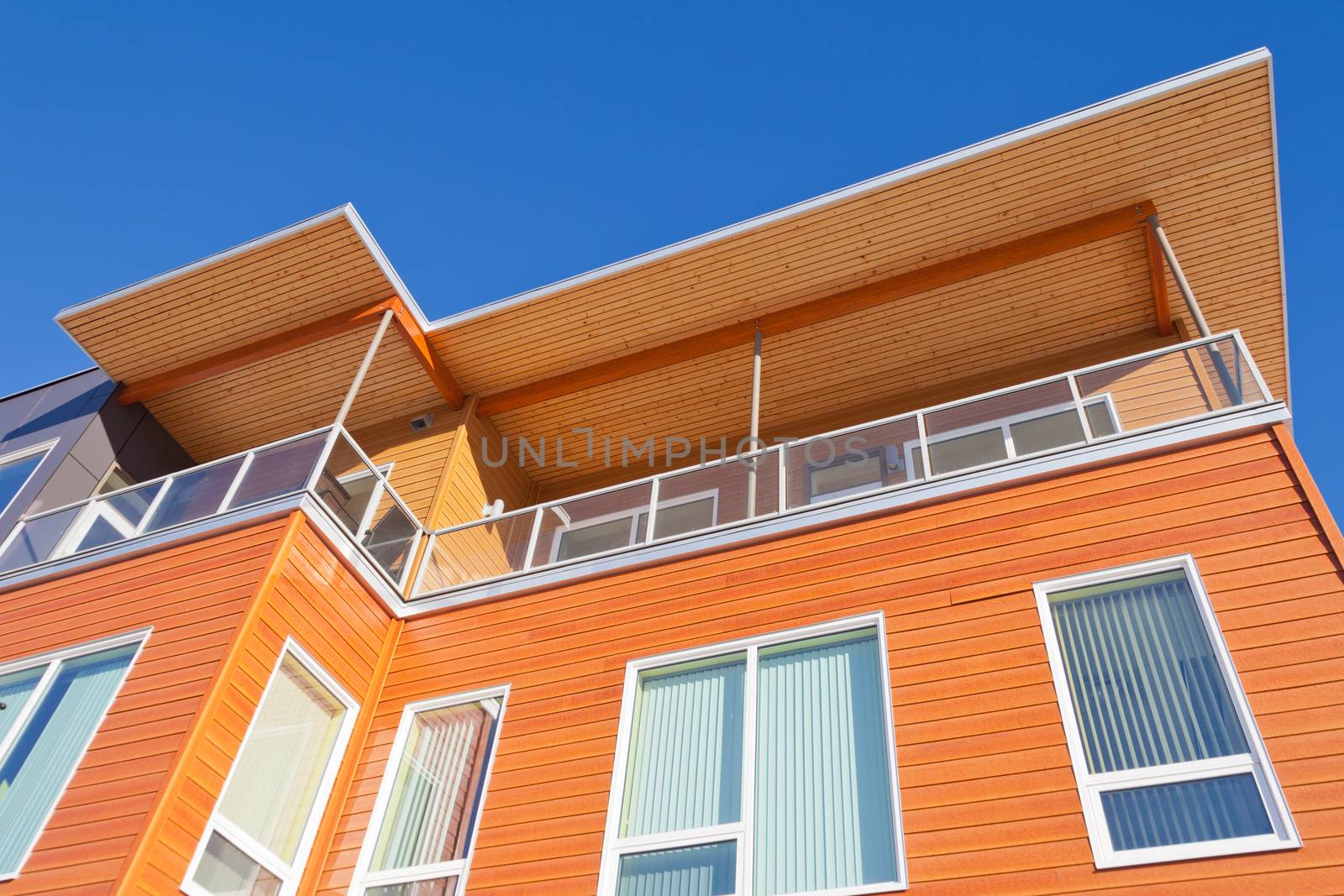 Upper storey detail of timber clad apartment building painted bright with penthouse balcony under blue sky