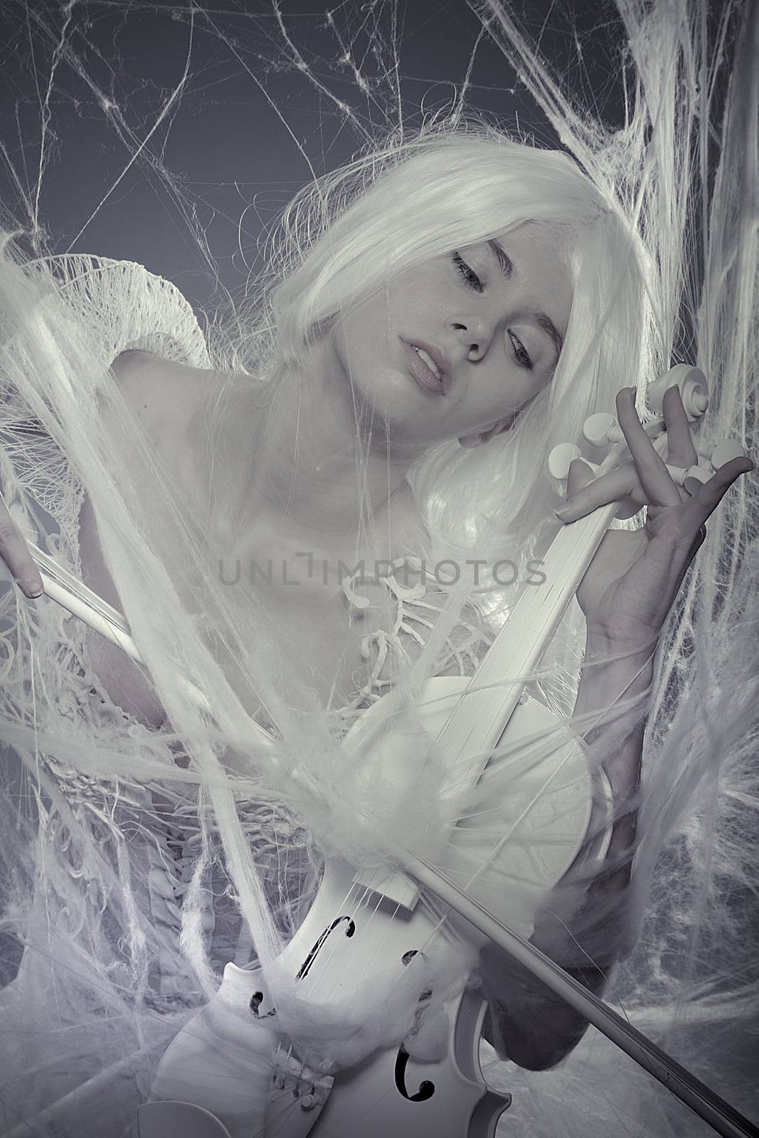 Fashion beautiful woman trapped in a spider web with a white violin, lace dress