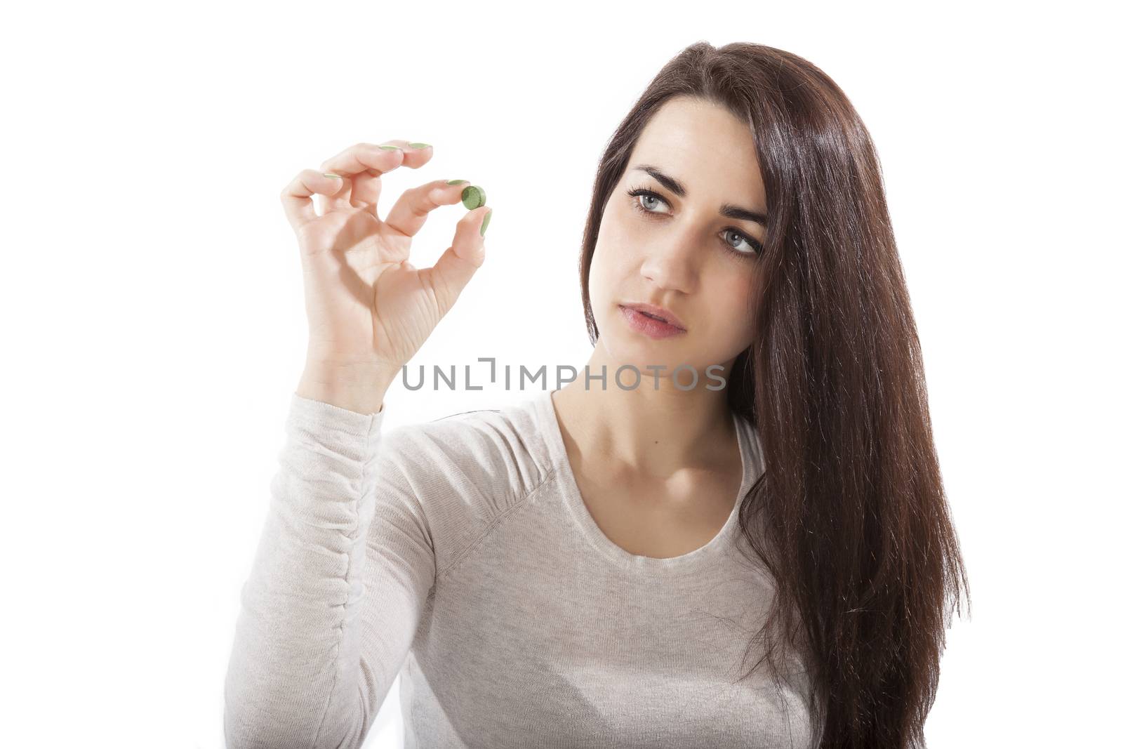 Beautiful girl in her 20s holding green chlorella and spirulina pill isolated on white background. Healthy eating, green superfood.