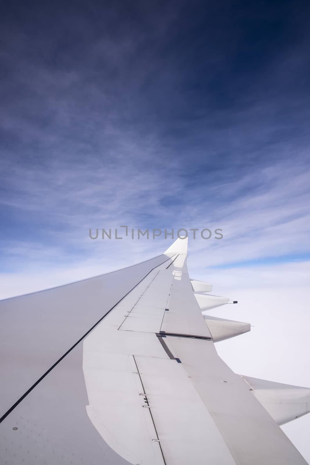 Wing of an airplane flying above the clouds by Yuri2012