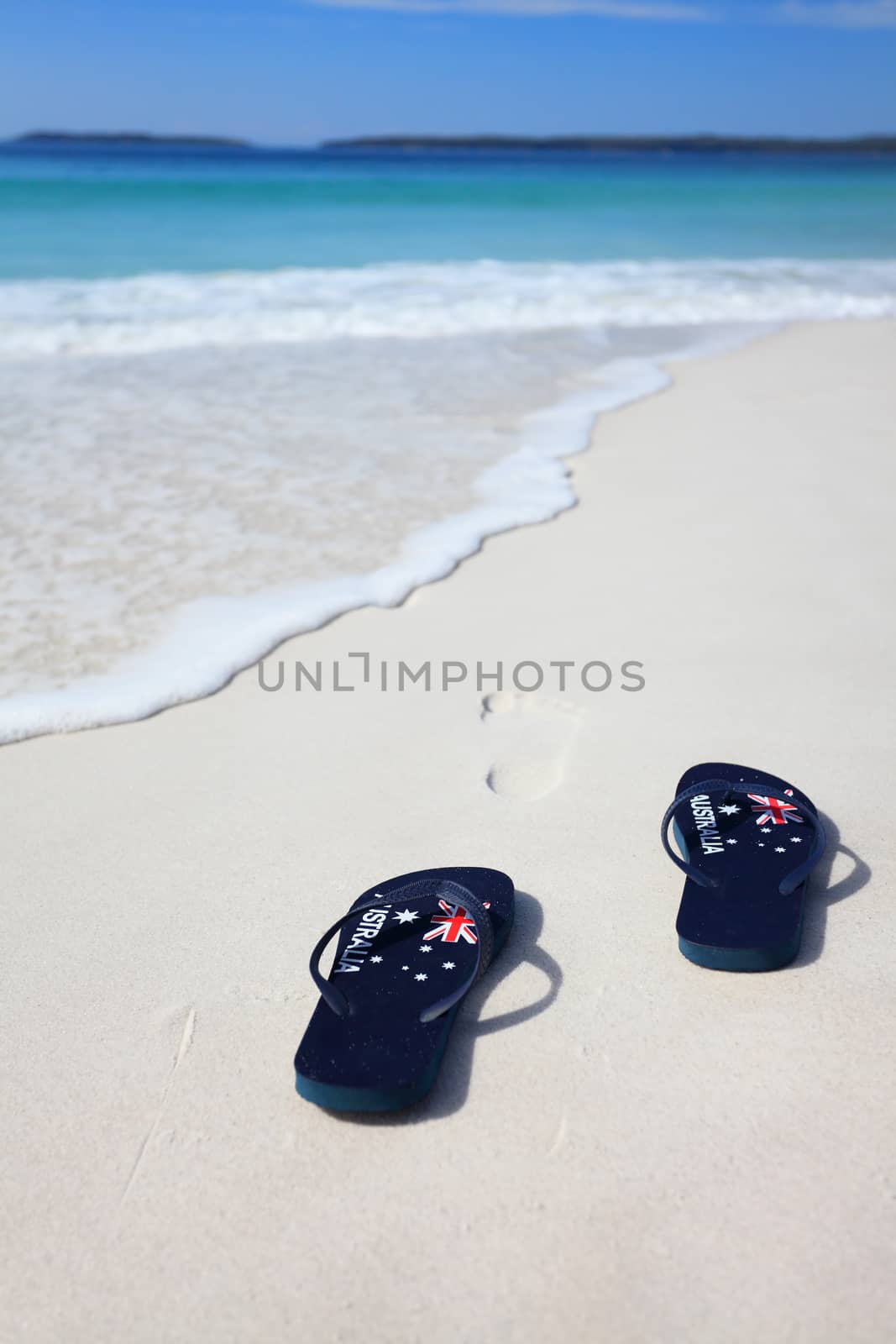 Australian flag thongs on the beach with footprints leading into the ocean.  Holiday, vacation, travel, leisure, unwind