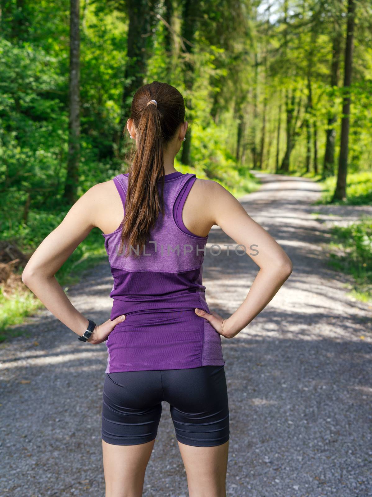 Photo of a young woman looking down the gravel path through a forest before she starts her exercise.