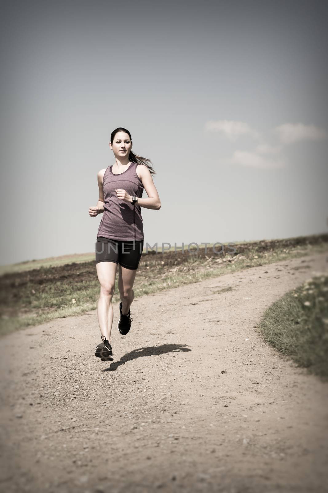 Photo of a beautiful young woman running down a gravel road. 