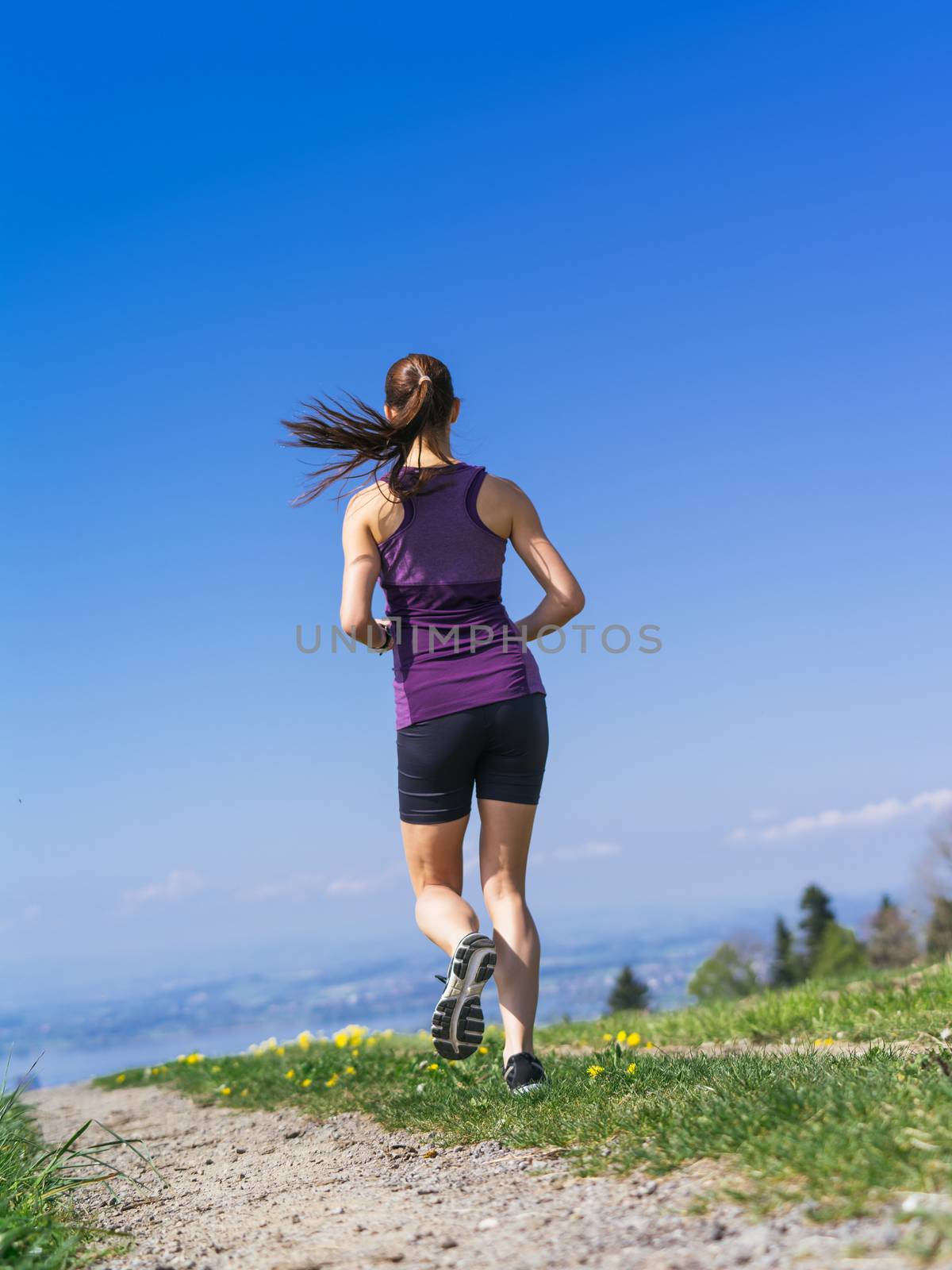 Photo of a young woman jogging and exercising on a country path.  Lake in the distance.