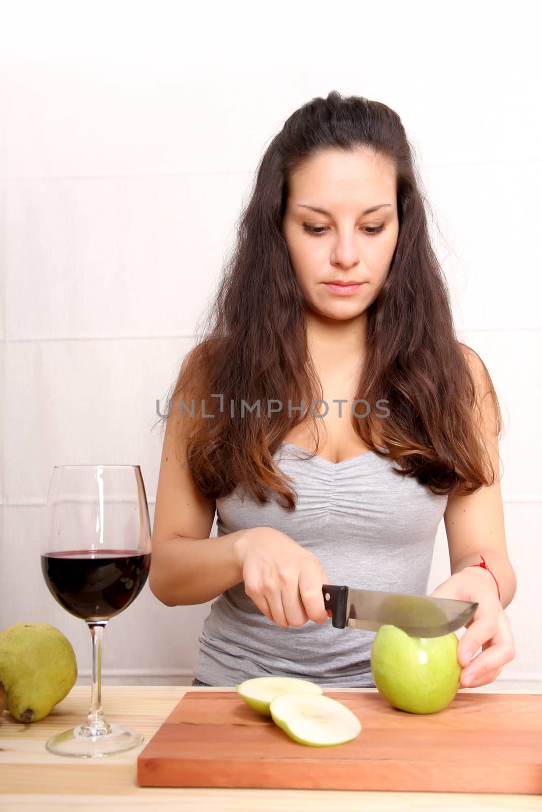 A young adult woman with fruits and wine in the kitchen.