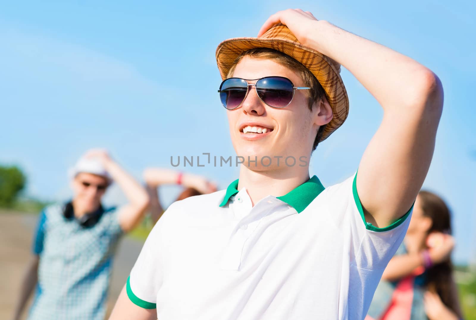 young man in sunglasses, a hat holds a hand on a background of blue sky and friends