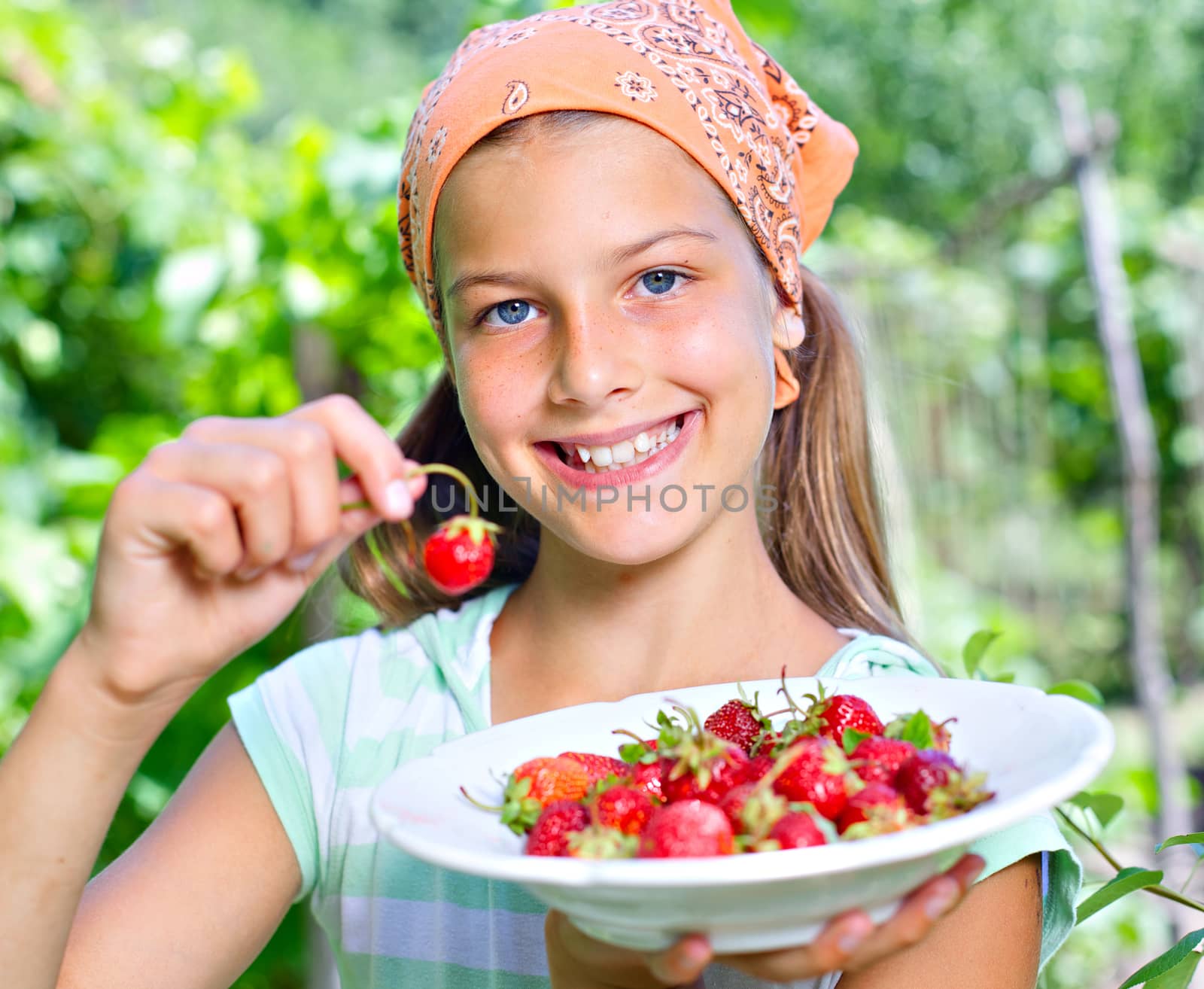 Happy cute girl in summer garden with plate of ripe fresh strawberries