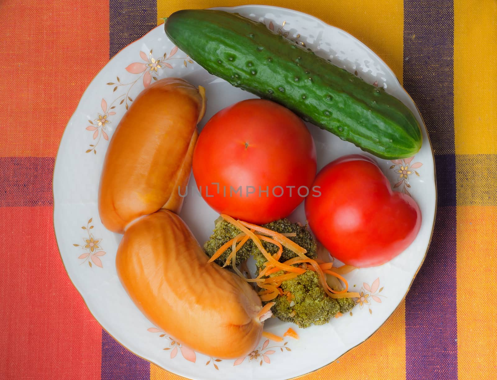 Two large appetizing sausages, tomatoes and cucumbers on a white dish. Are located on a slope