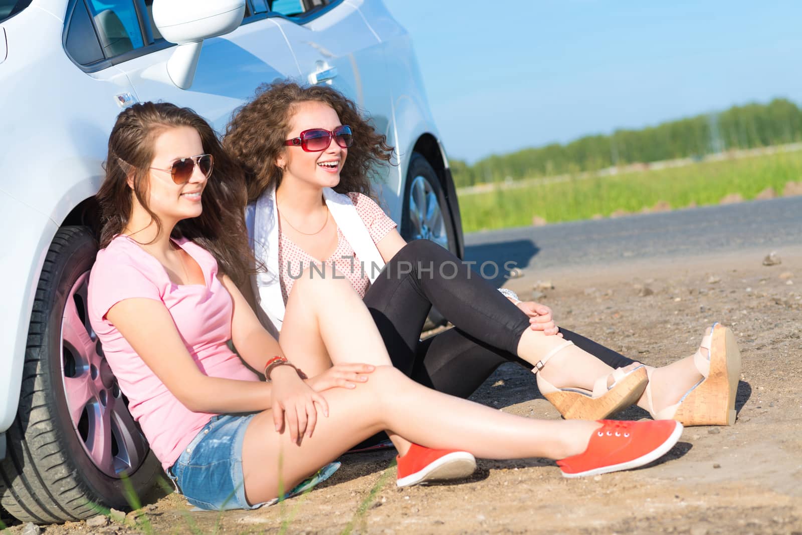 Two attractive young women wearing sunglasses, sitting next to the car