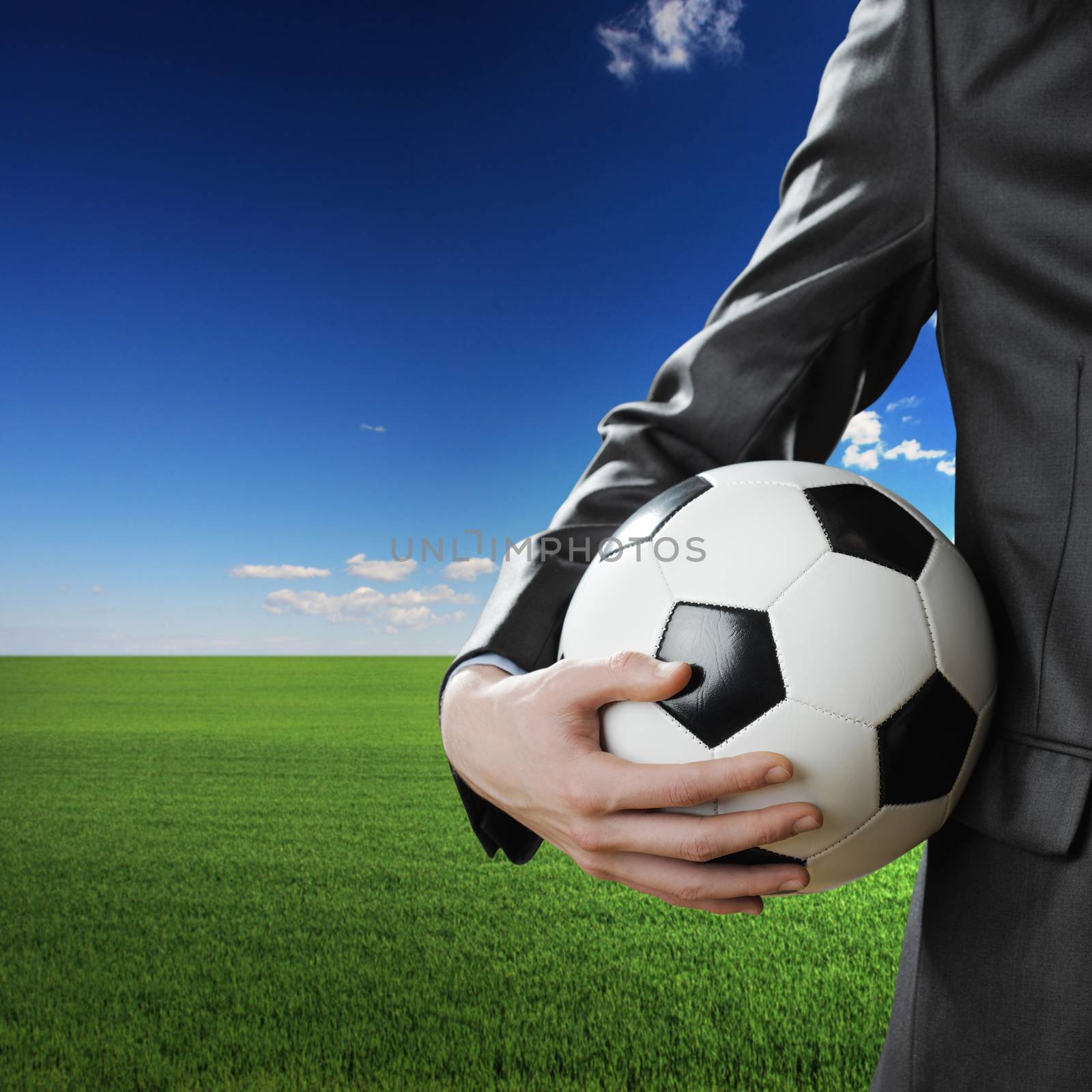 Businessman holding a soccer ball with blue sky and green meadow on background.