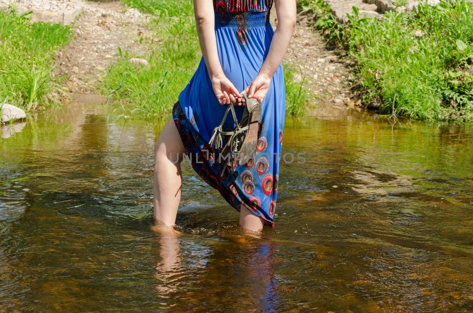 female legs with blue dress standing wade into the fast flowing stream summer nature park