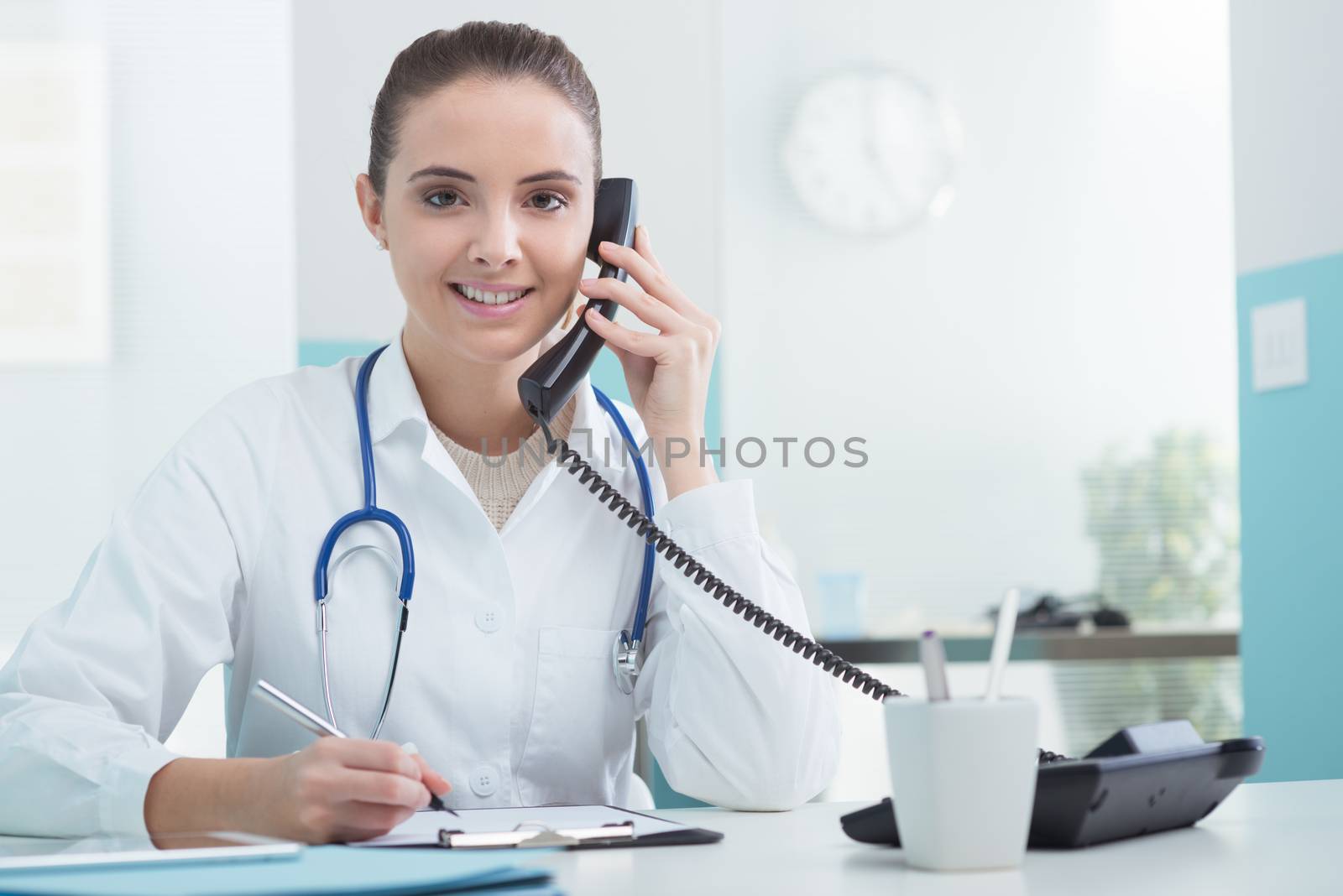 Young female doctor sitting at her desk and talking on the phone