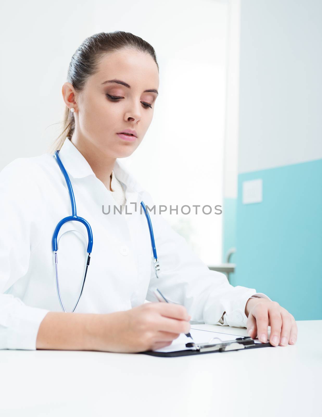 Young woman doctor or pharmacist in office writing on clipboard