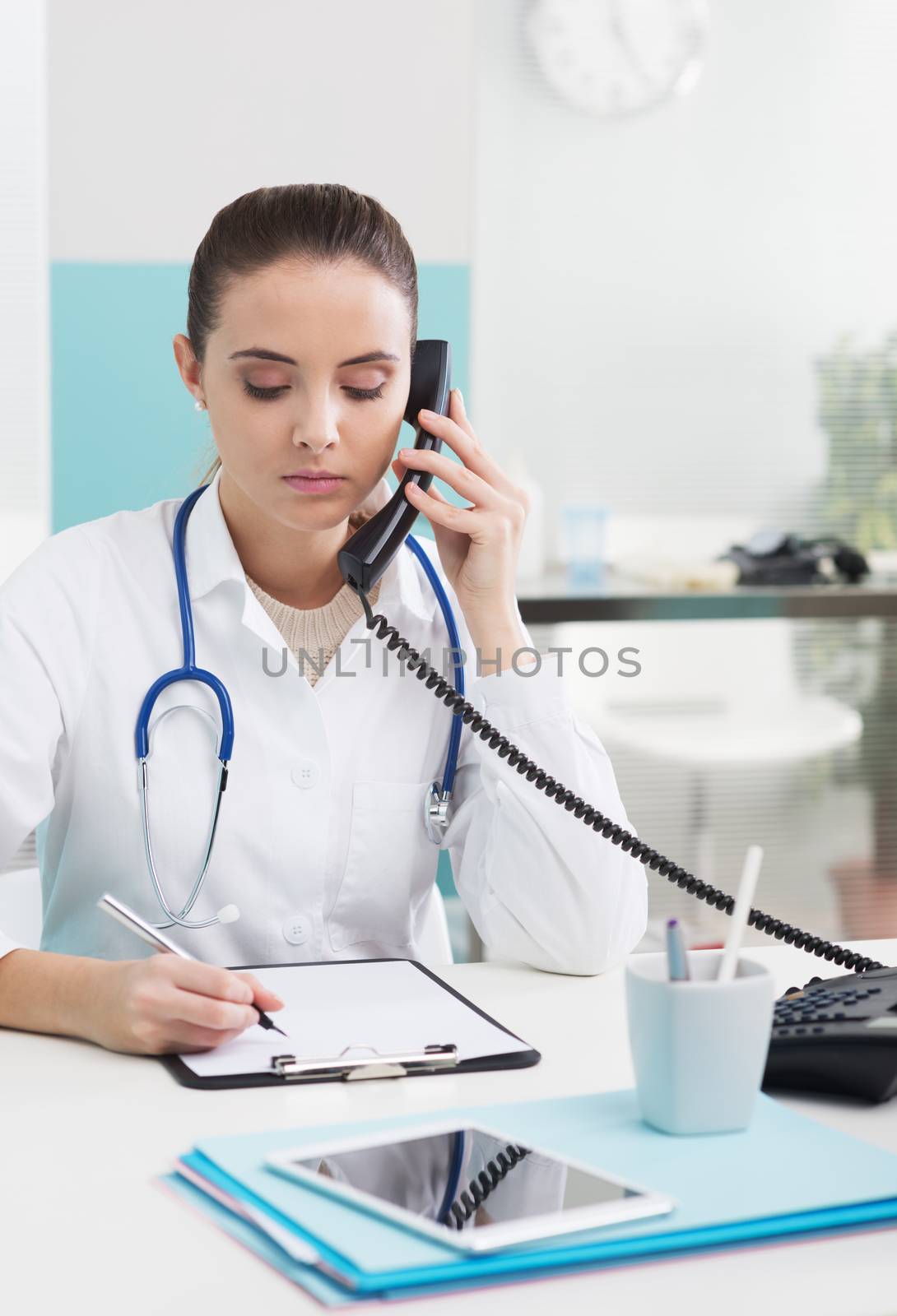 Young female doctor sitting at her desk and talking on the phone