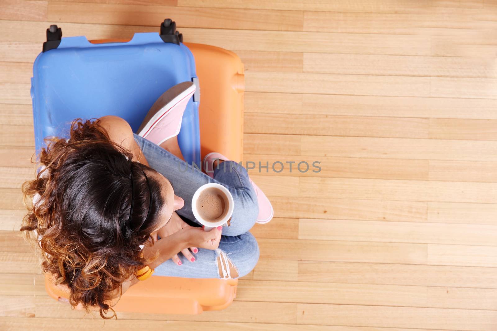 A young woman sitting on a stack of suitcases while drinking coffee and waiting for the departure to vacations.