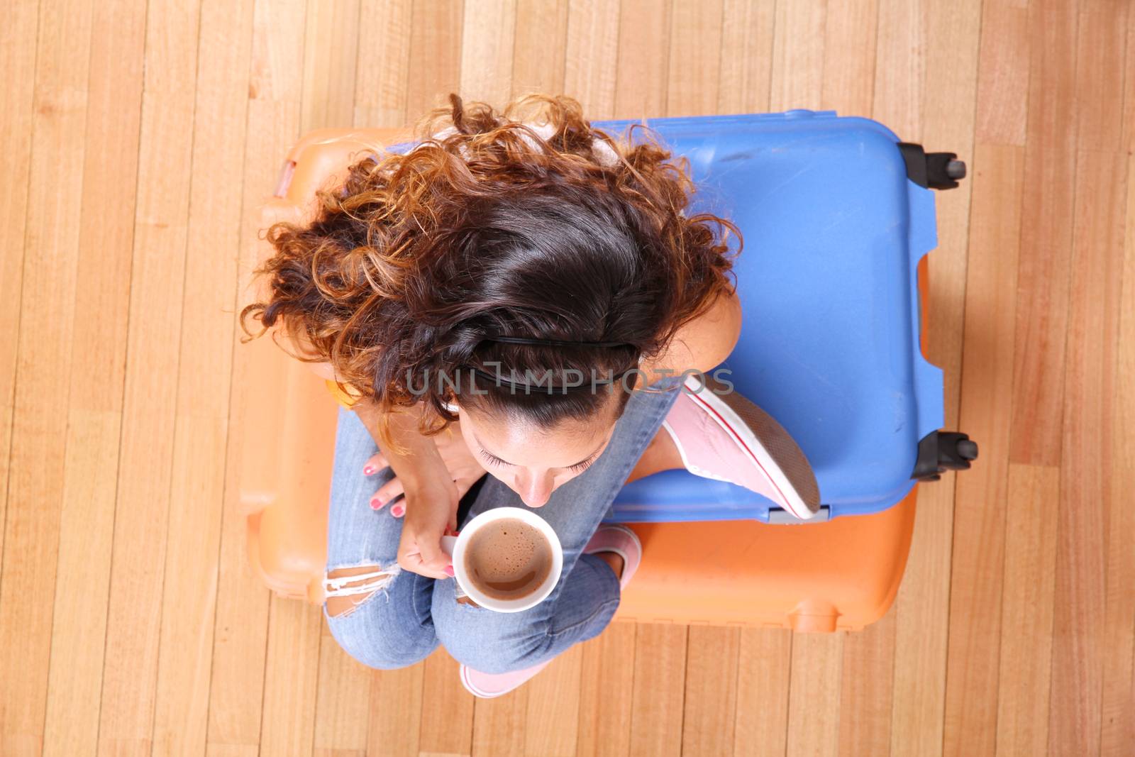 A young woman sitting on a stack of suitcases while drinking coffee and waiting for the departure to vacations.