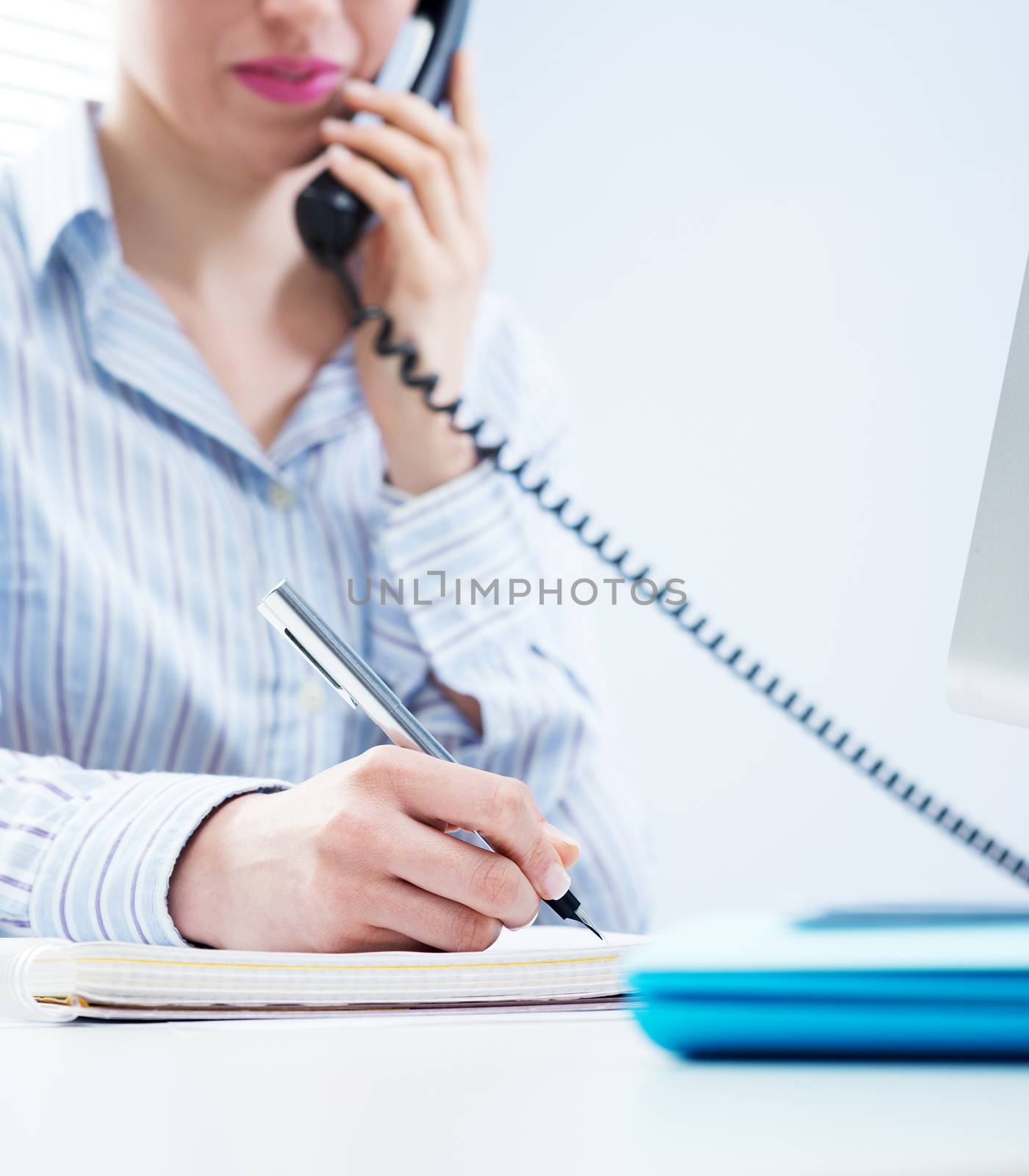 Woman working on the phone and writing down notes at office.