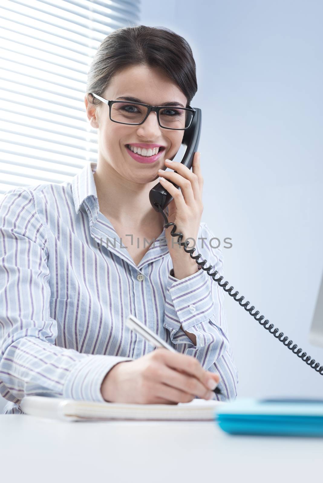 Beautiful woman with glasses answering phone calls at desk.