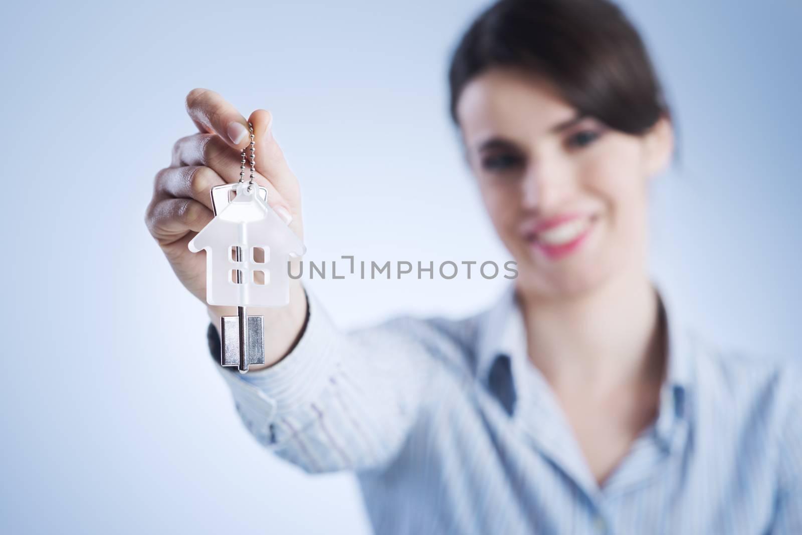 Real estate agent holding out house keys and smiling.