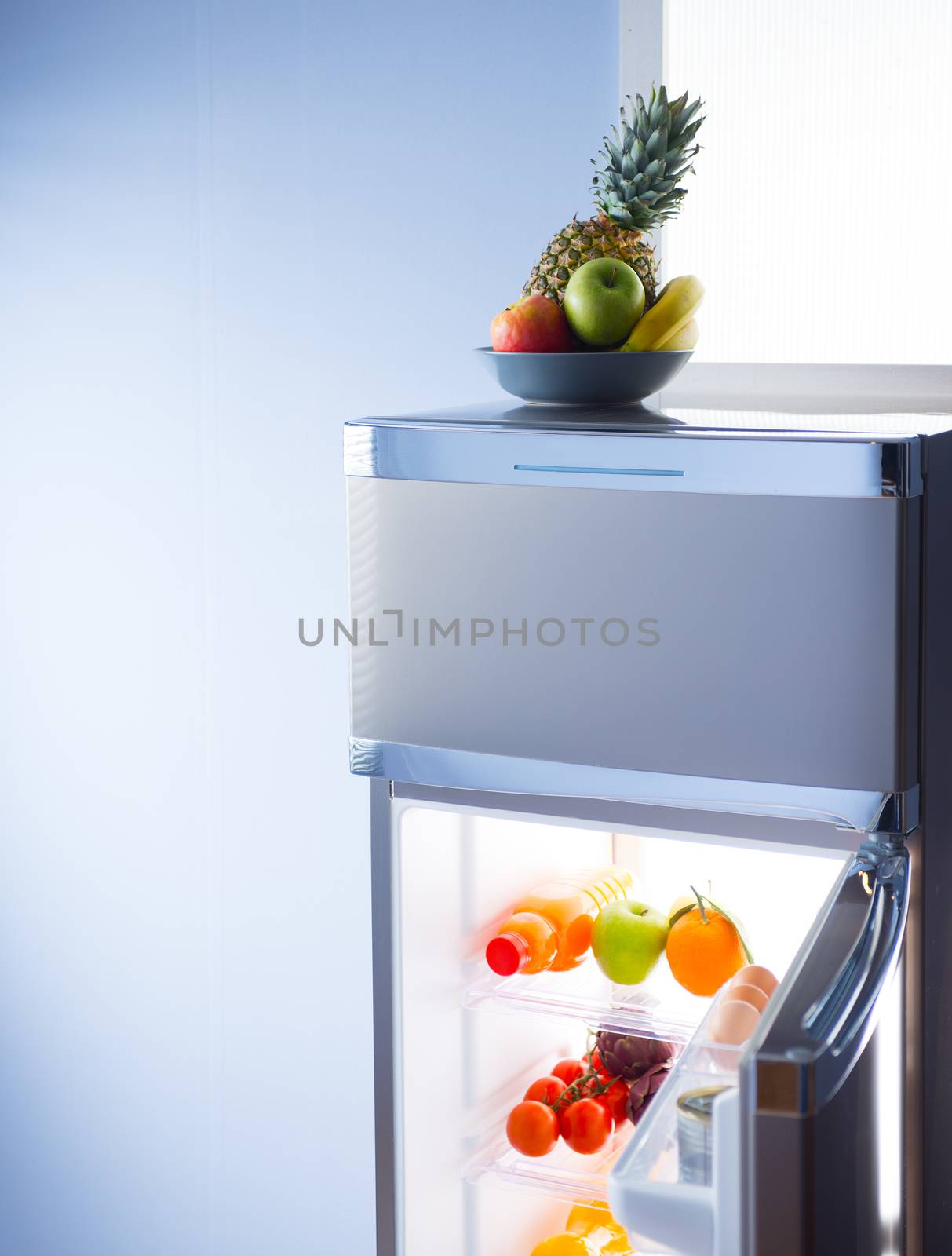 Fruit bowl and open refrigerator with healthy food on shelves.