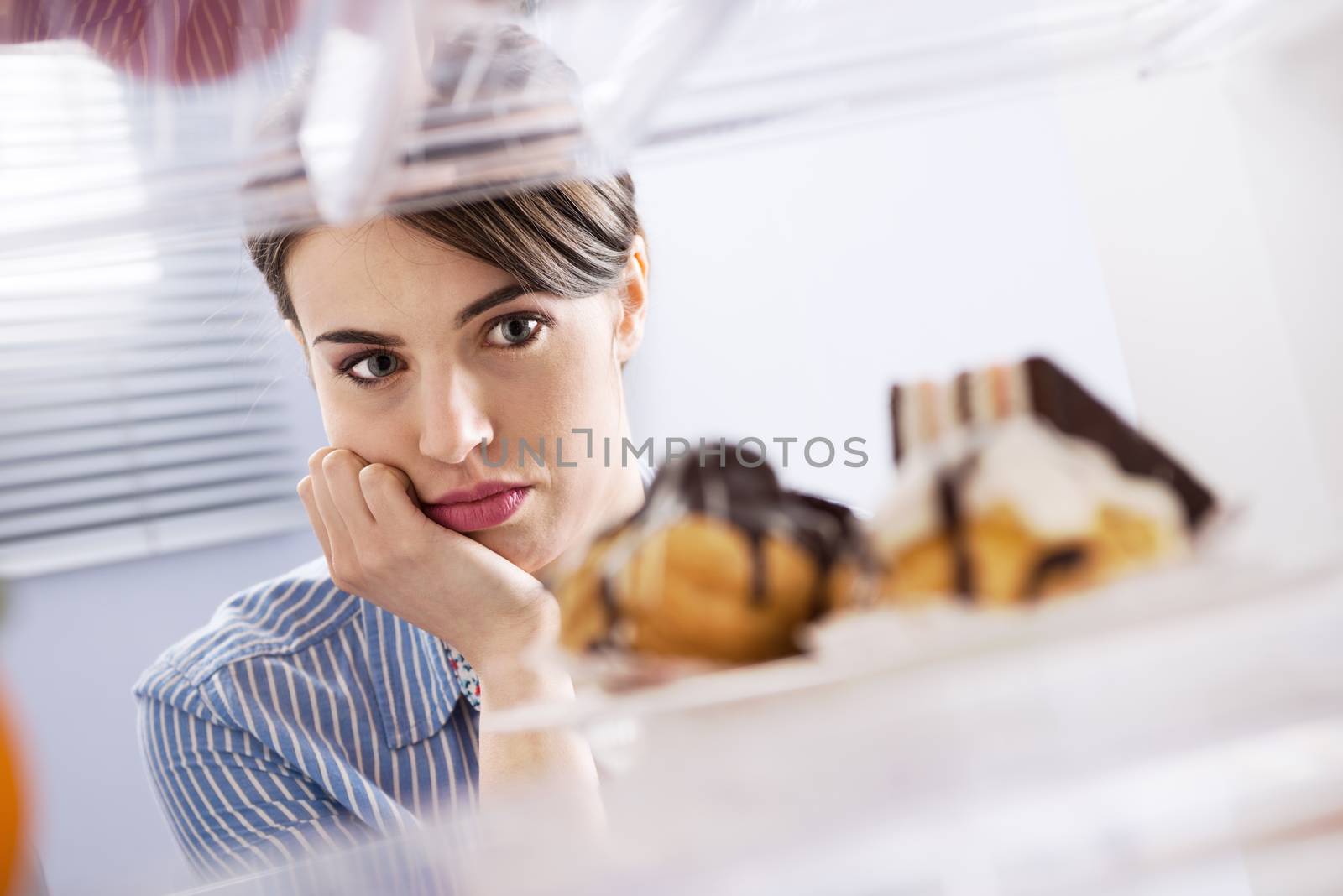 Young hungry woman in front of refrigerator craving chocolate pastries.