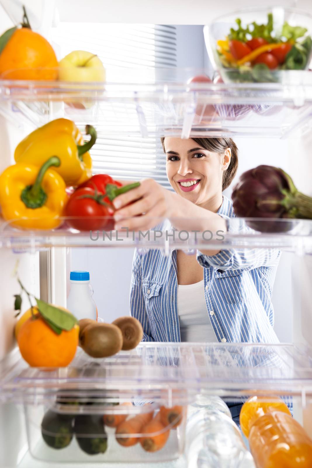 Young woman taking fresh healthy vegetables from refrigerator.