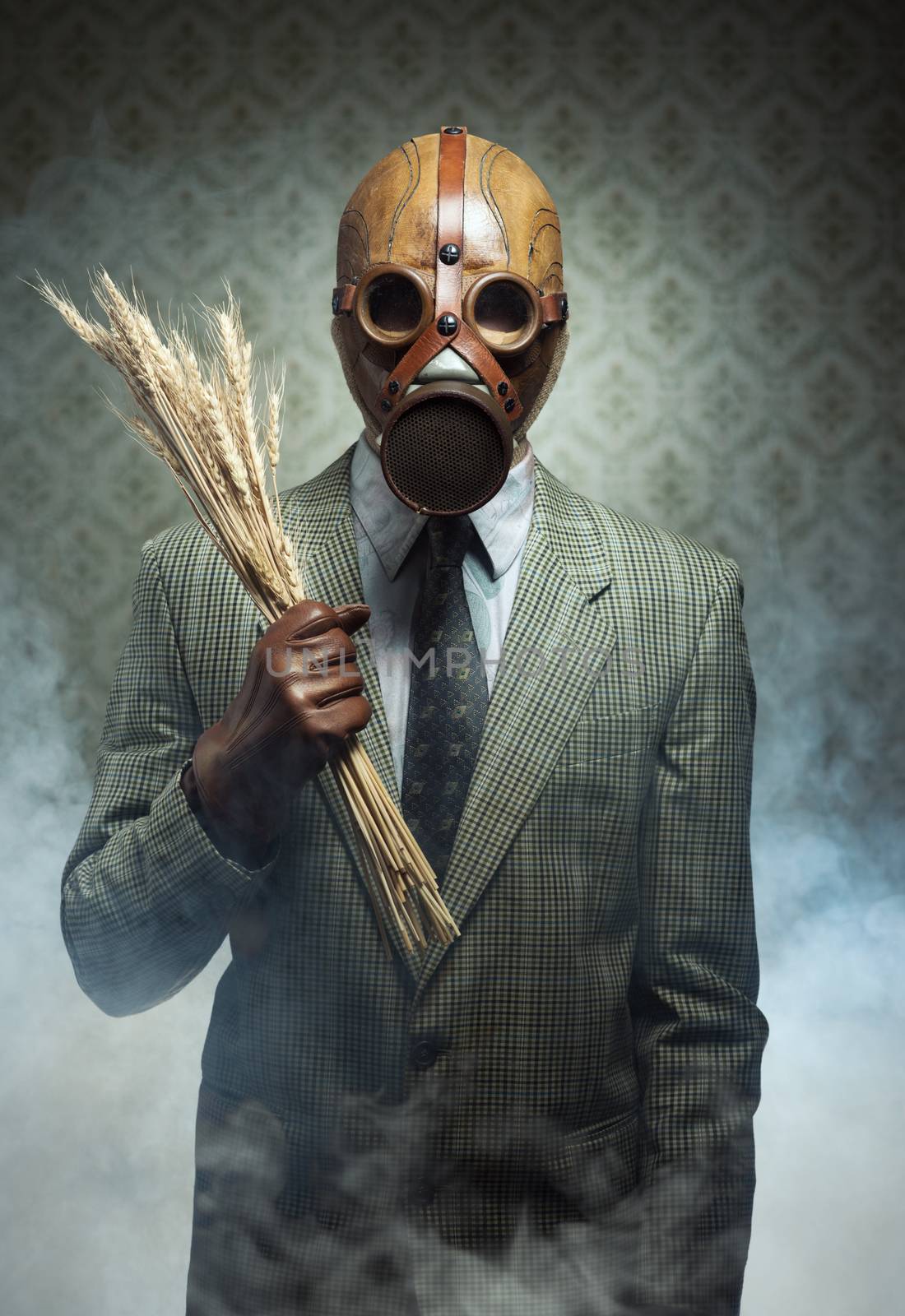 Man wearing a gas mask and holding ears of wheat with toxic smoke on background.