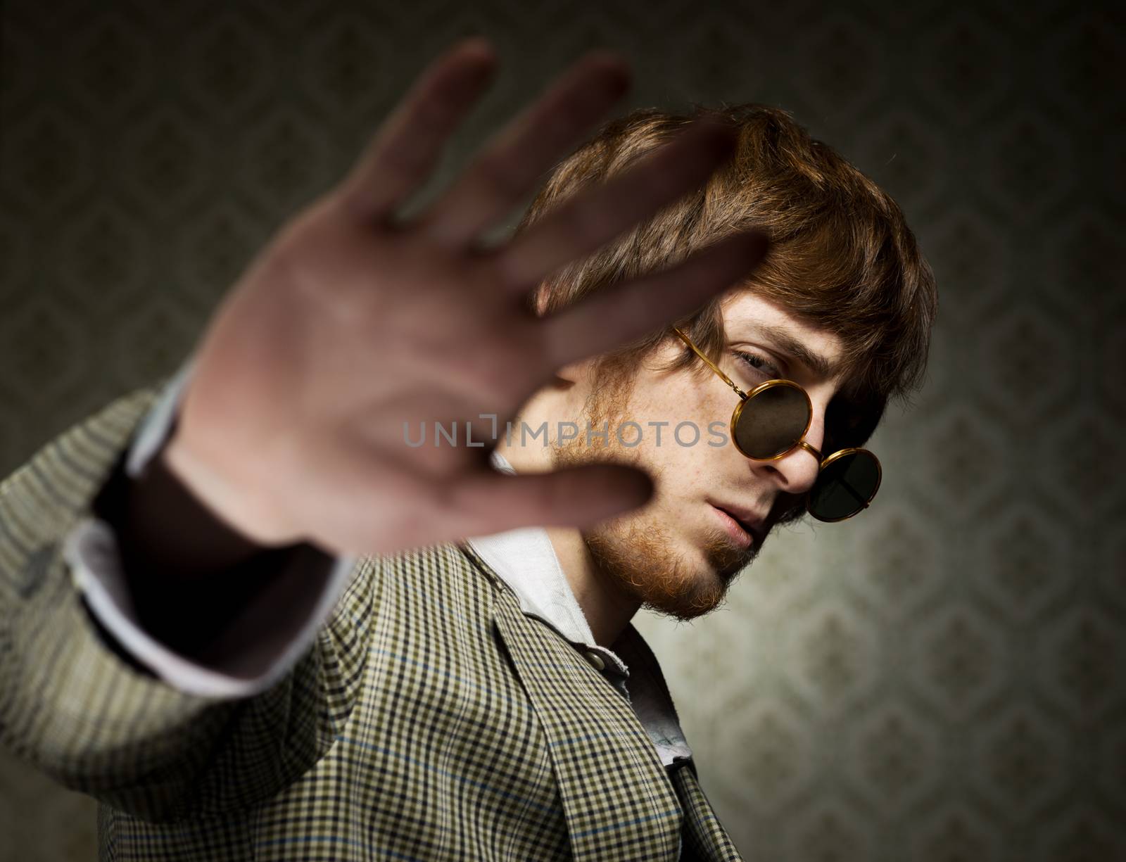 1960s style guy posing with circular glasses on vintage wallpaper background.