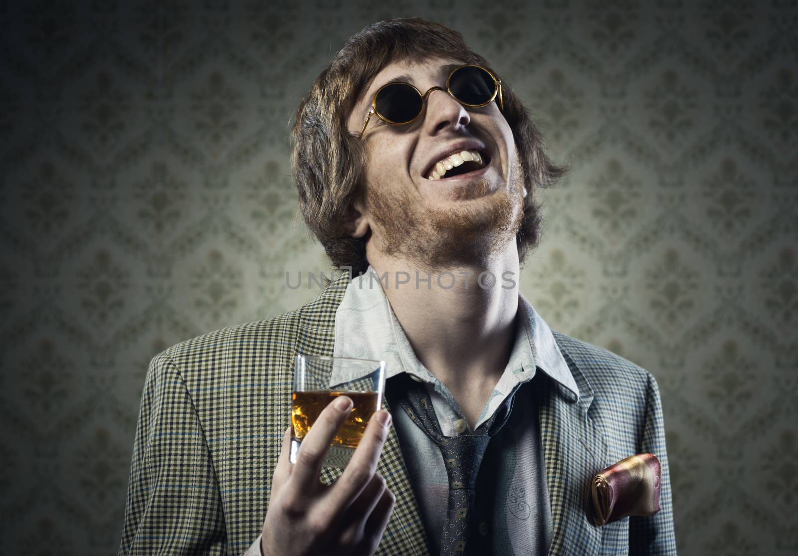 Funny guy holding a glass of whisky and posing against vintage wallpaper.