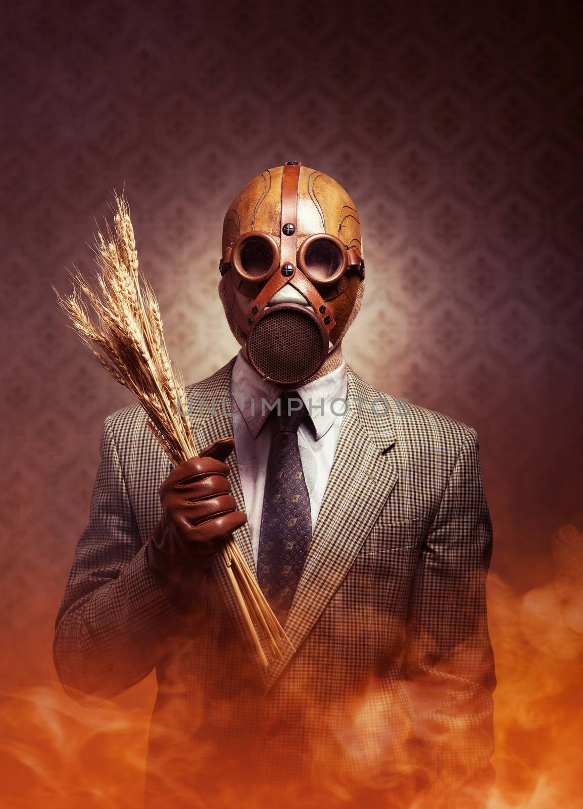 Man wearing a gas mask and holding ears of wheat with toxic smoke on background.