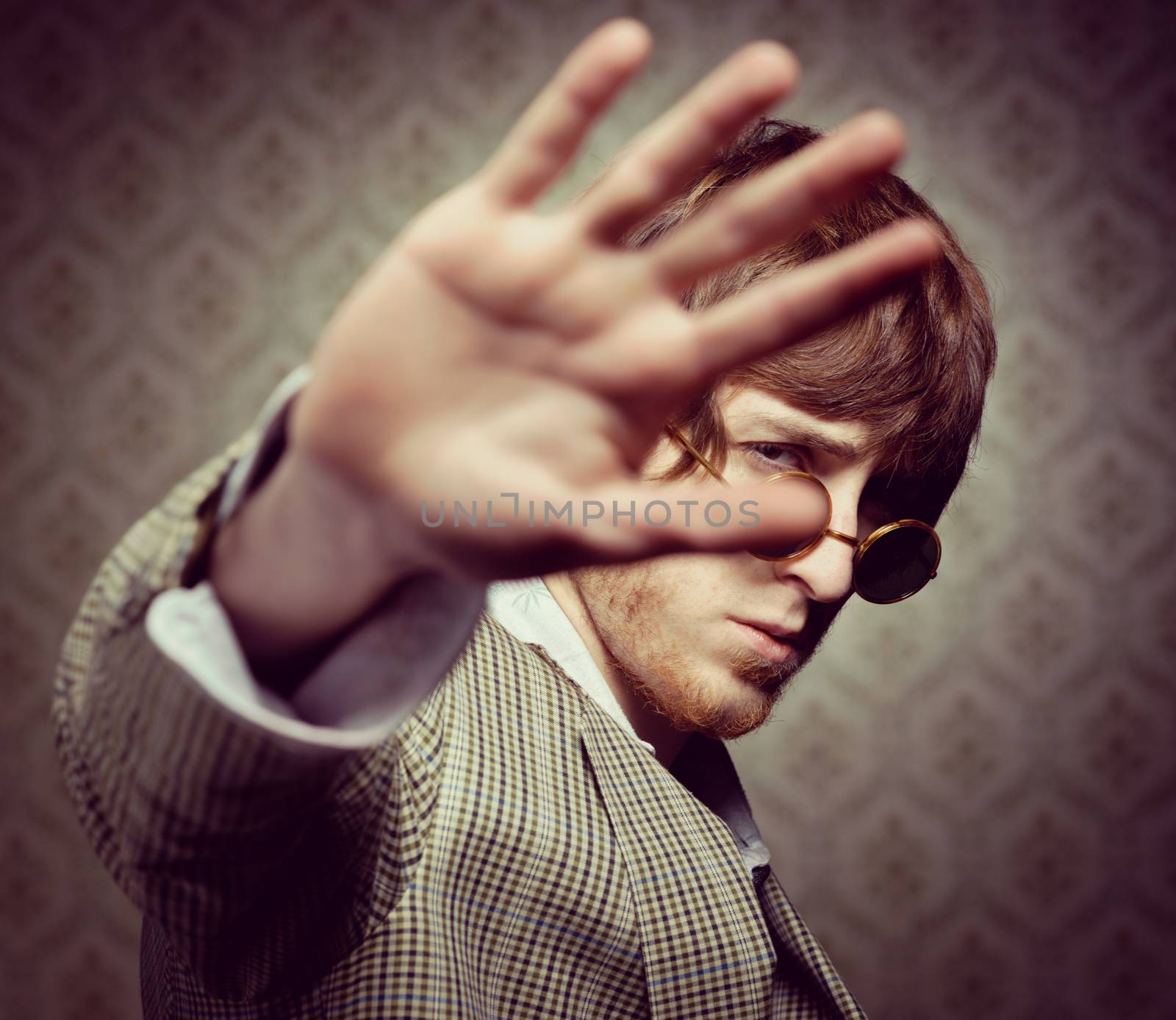 1960s style guy posing with circular glasses on vintage wallpaper background.