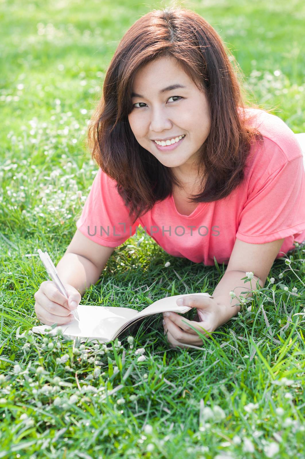 Happy Young Asian Woman Writing in Notebook and Smiling in Spring Garden.