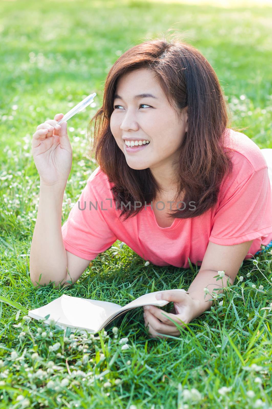 Happy Young Asian Woman Writing in Notebook and Smiling in Spring Garden.