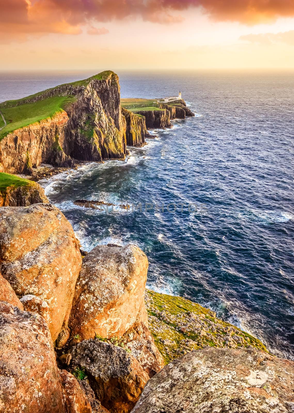 Vertical view of Neist Point lighthouse with rocks in foreground and rocky coastline, Scotland
