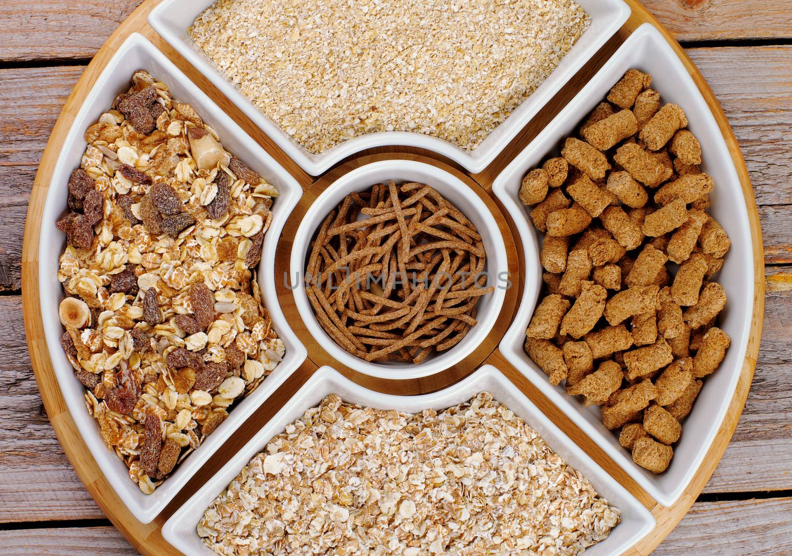 Various Muesli, Oat Flakes and Bran in White Plates closeup on Wooden background