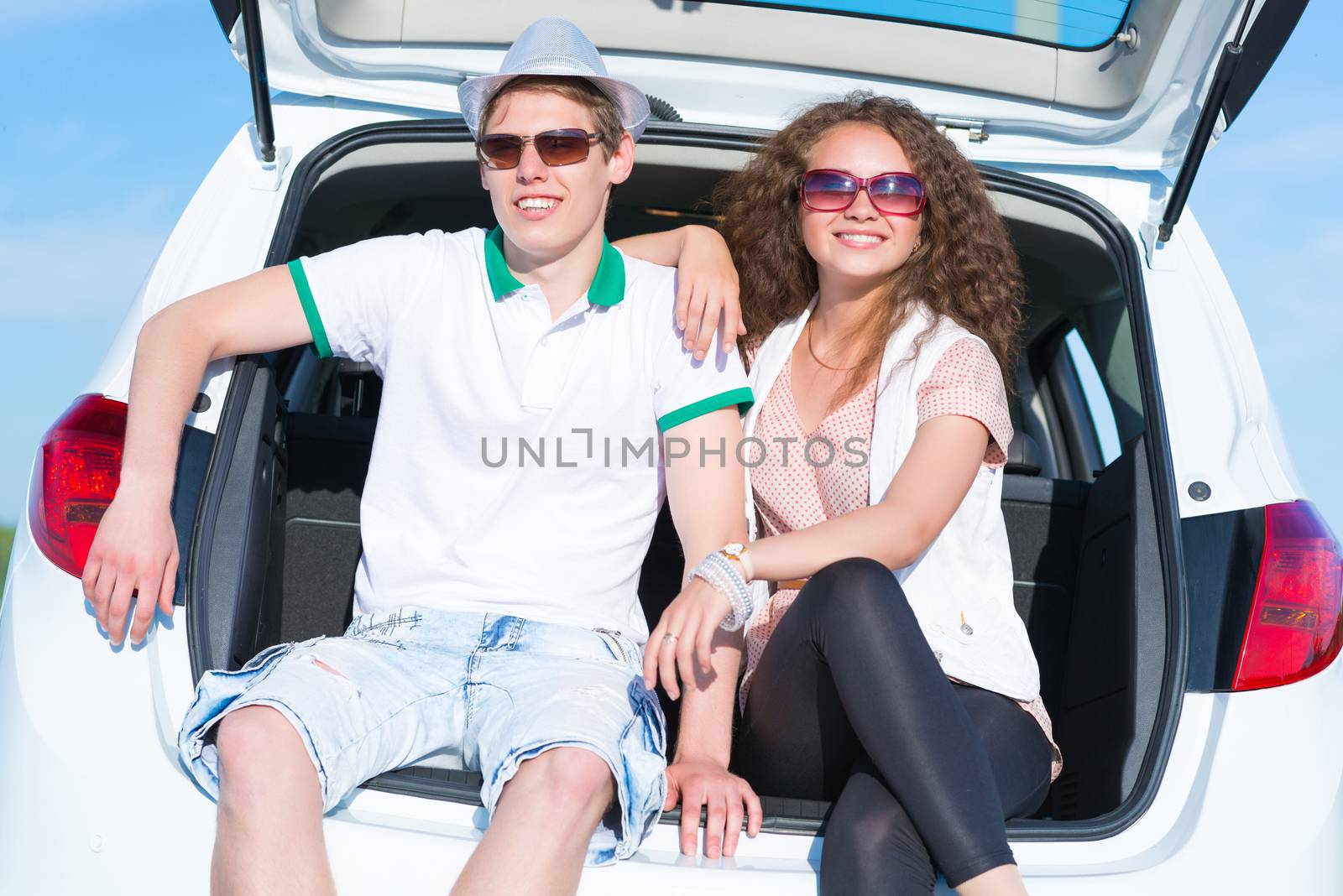 young couple sitting in the open trunk of a new car, a summer road trip