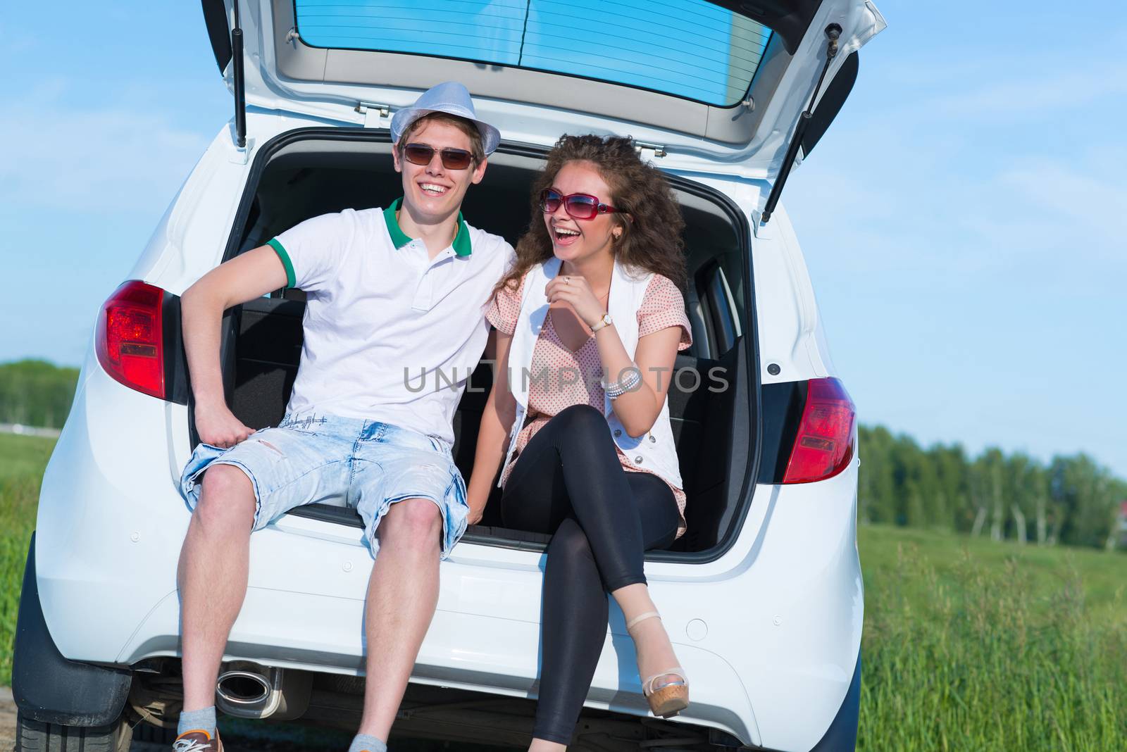 young couple sitting in the open trunk of a new car, a summer road trip