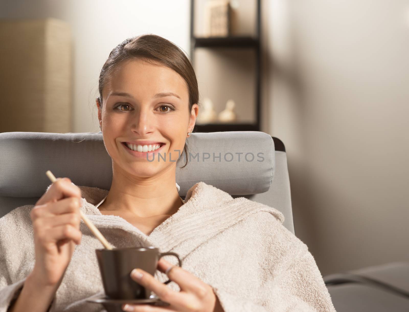 Young woman smiling and relaxing at spa, holding an hot healthy drink.