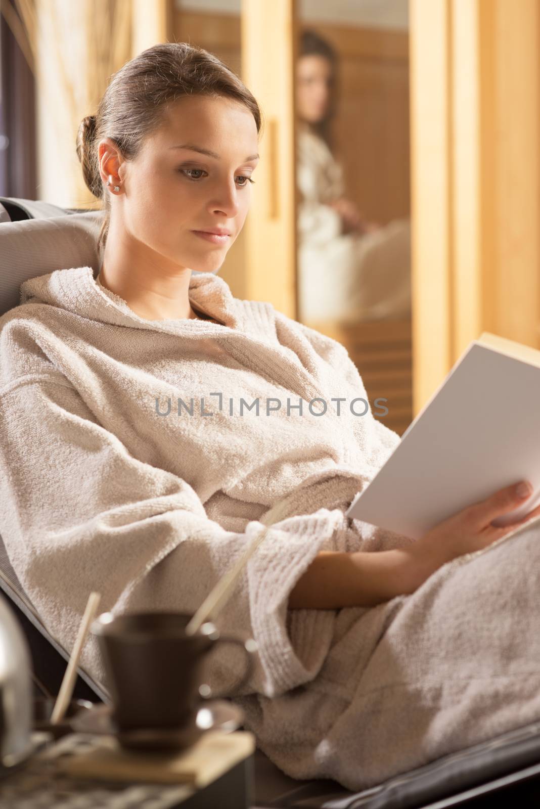 Young woman in bathrobe relaxing at spa and reading a book.