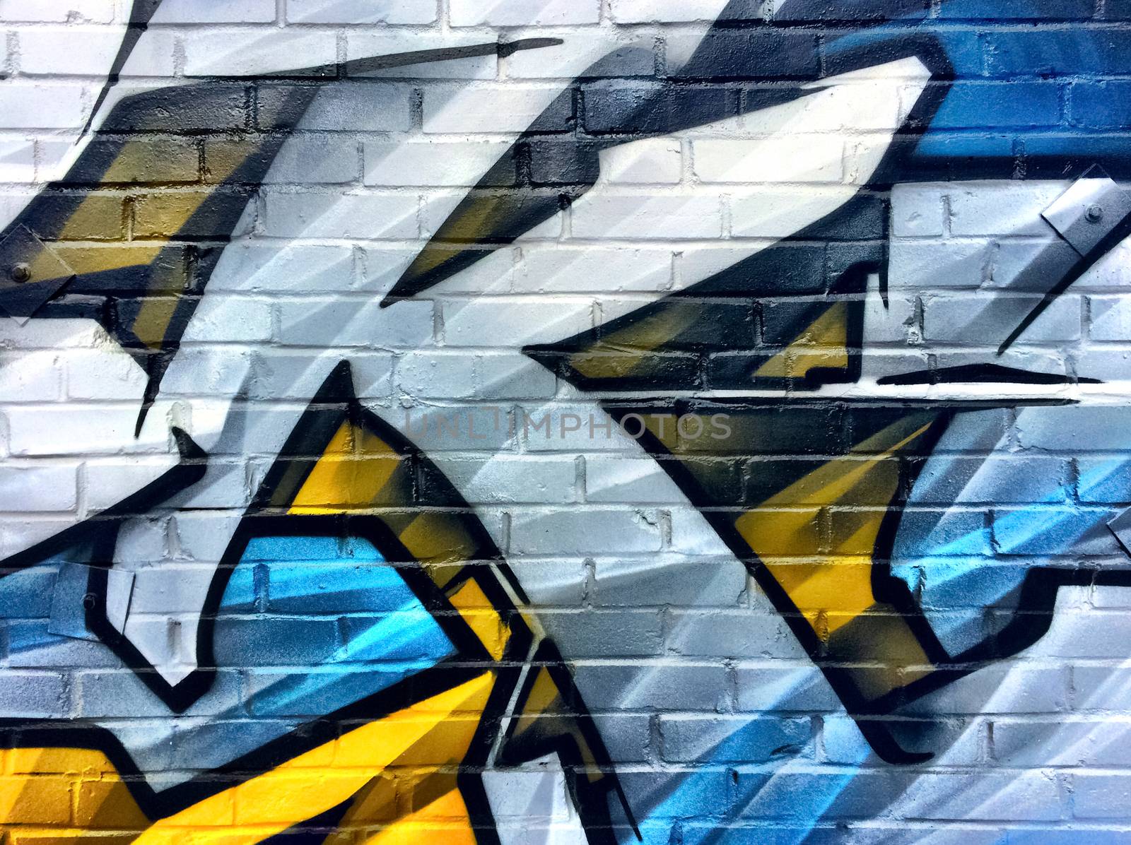 Blue and yellow graffiti detail on a brick wall by anikasalsera